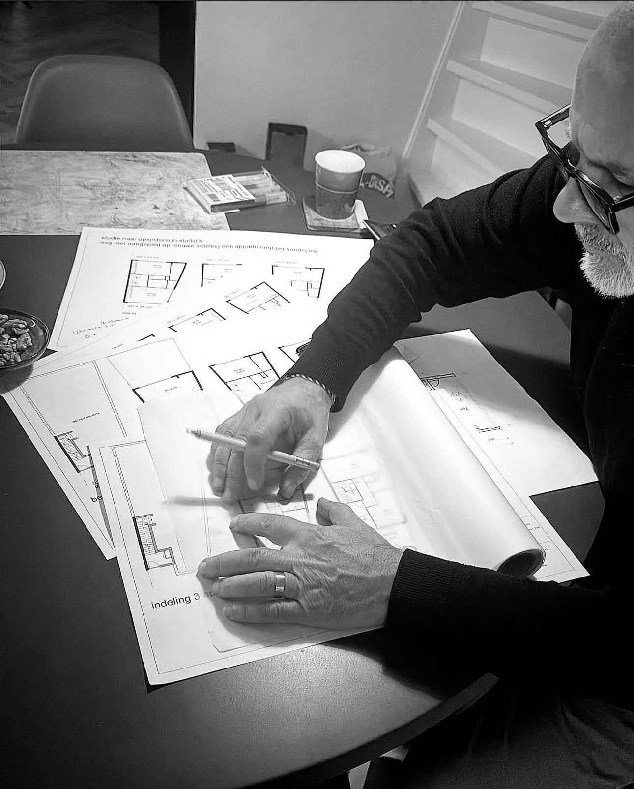 Sertan Özbudun at his drawing table, pencil in hand, floor plans spread before him.